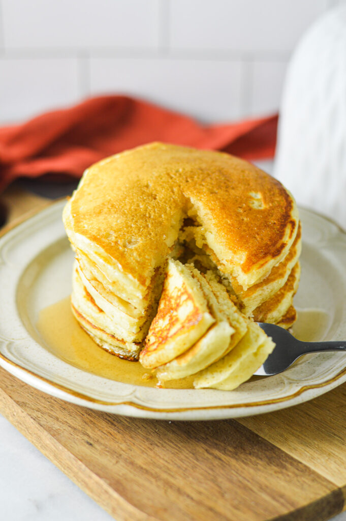 A stack of fluffy Plain Pancakes, with a wedge slice taken out on a fork, showing the soft center.