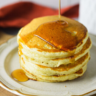 A stack of golden Plain Pancakes, with a drizzle of maple syrup coating the top.