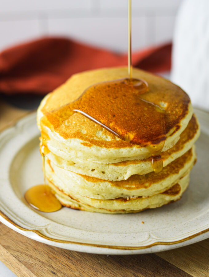 A stack of golden Plain Pancakes, with a drizzle of maple syrup coating the top.