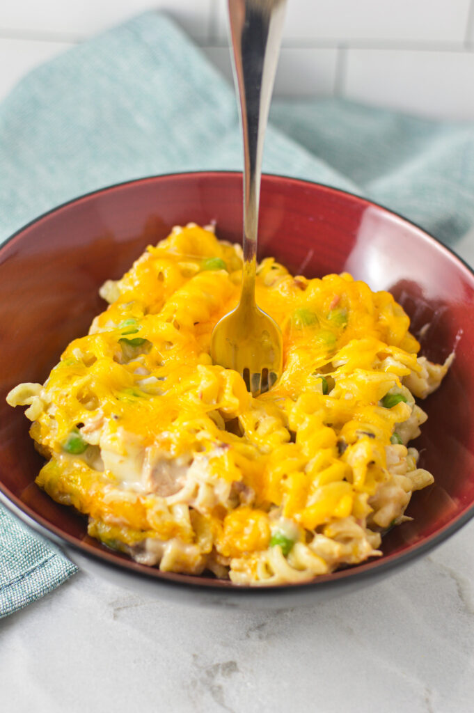 A small bowl full of cheesy Tuna Casserole with a fork sticking out of it, showing its thick, hearty texture.