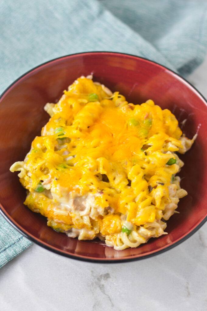 Tuna Casserole in a small red bowl covered in melted cheddar cheese.