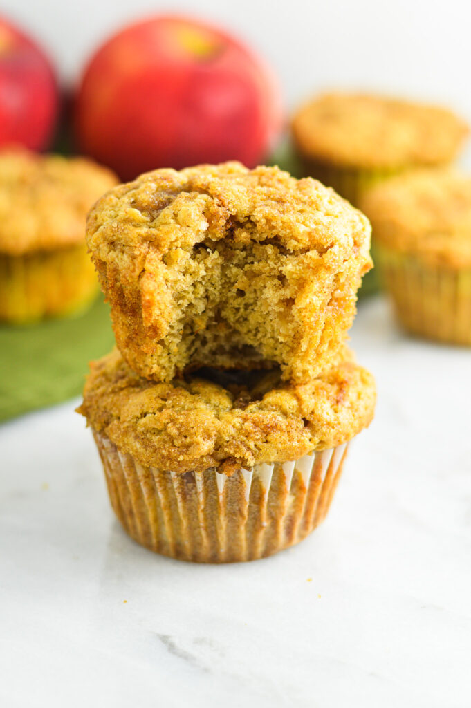 A stack of two Apple Streusel Muffins with a bite taken out of the top muffin revealing a moist interior filled with apple chunks.