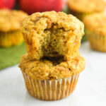 A stack of soft Apple Streusel Muffins with a bite taken out of the top muffin, revealing chunks of tender apples in the moist interior.