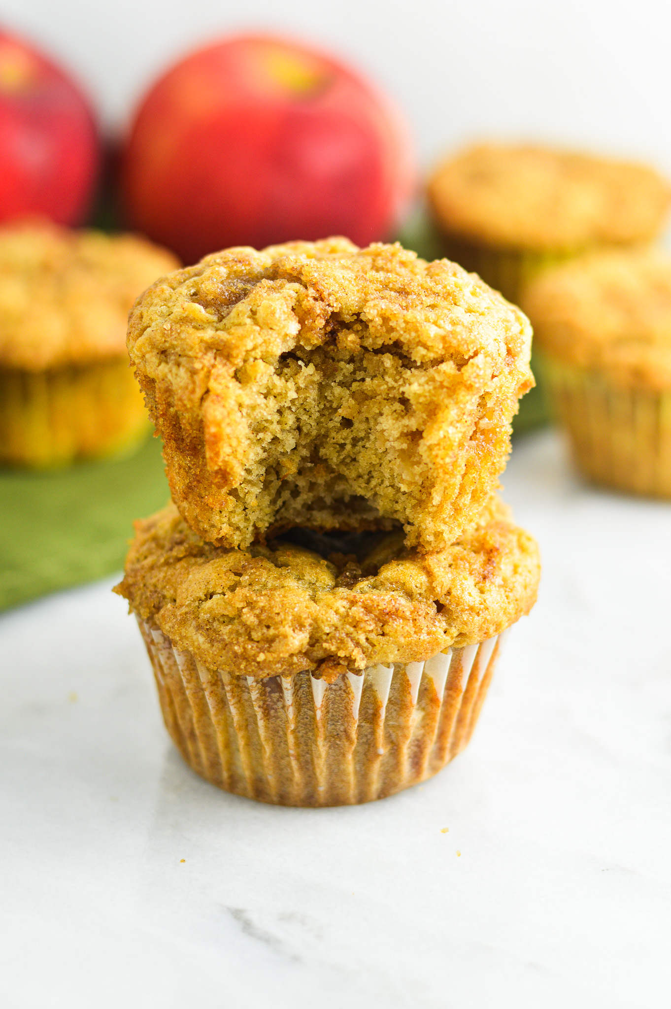 A stack of soft Apple Streusel Muffins with a bite taken out of the top muffin, revealing chunks of tender apples in the moist interior.