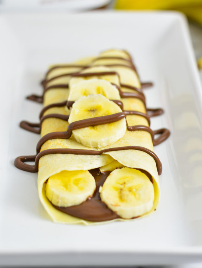 Banana and Nutella filled crepe with Nutella drizzle on a white rectangular plate.