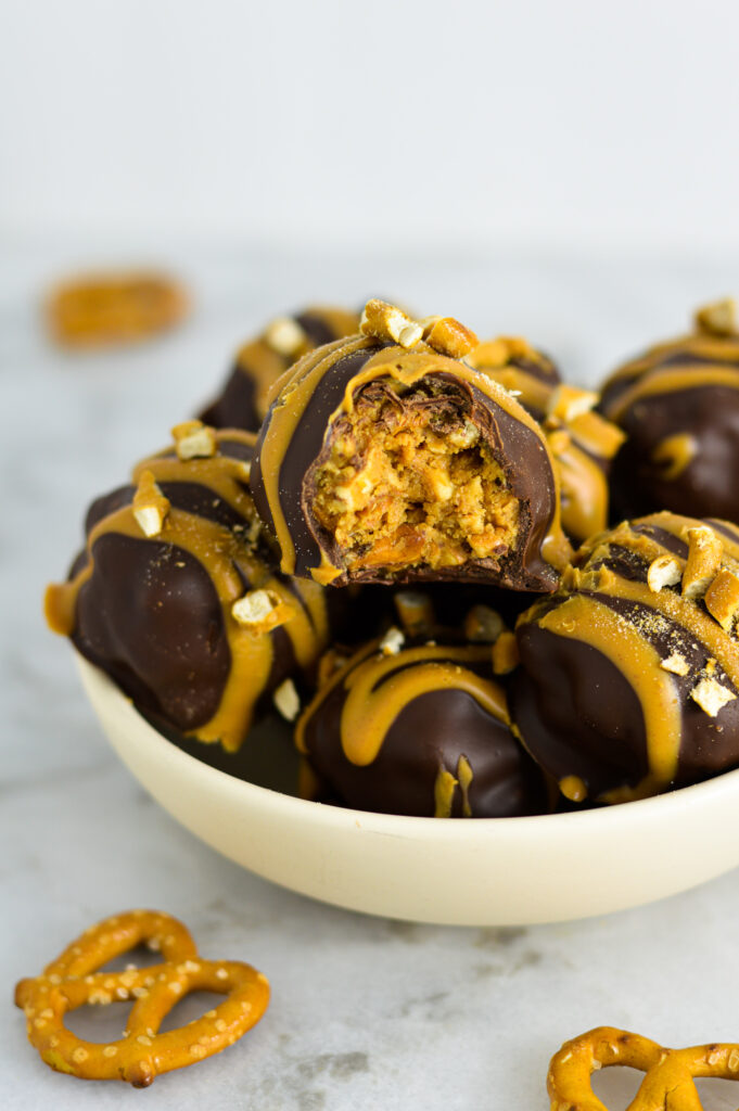 A small bowl of Peanut Butter Pretzel Truffles with a bite taken out of one of them.