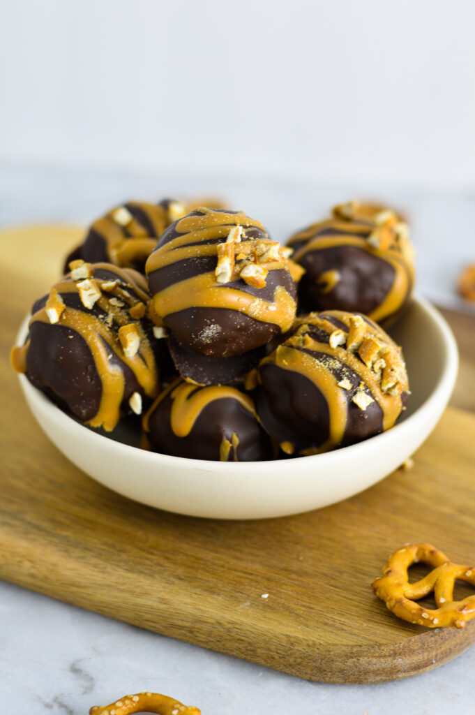 A shallow bowl full of Peanut Butter Pretzel Truffles on a small cutting board.