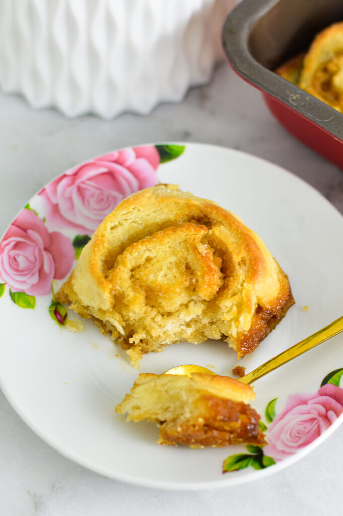 A butterscotch pinwheel on a small flowered plate along with a gold spoon.