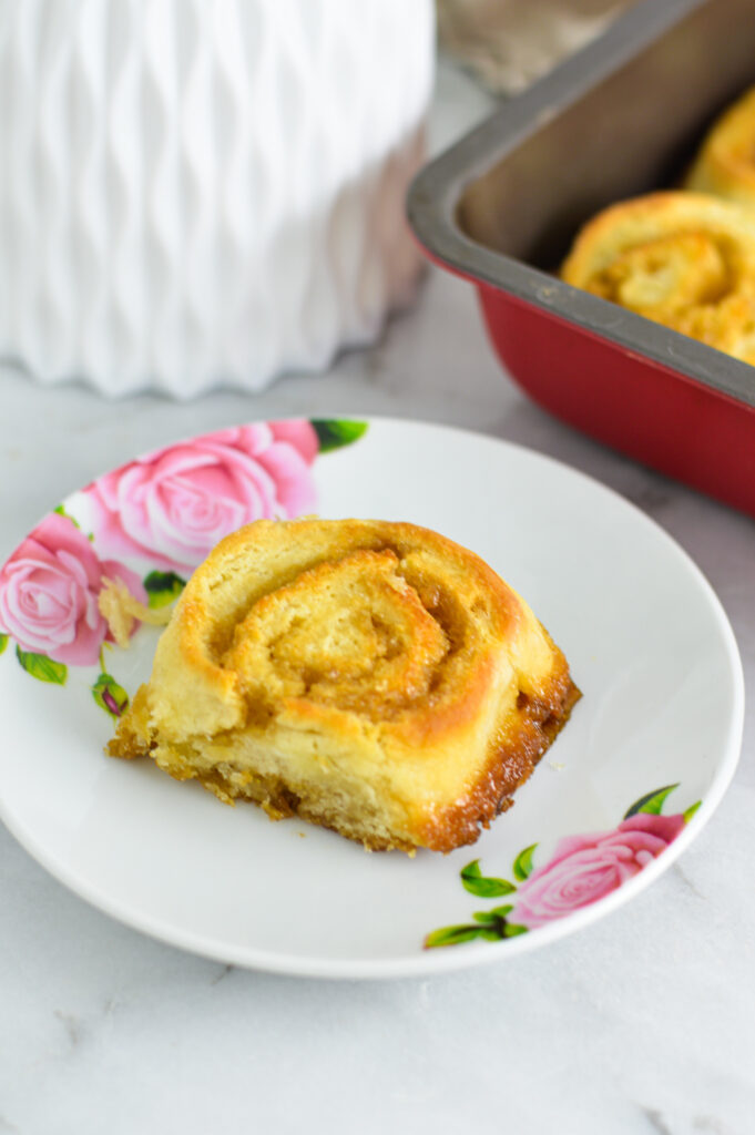 One butterscotch pinwheel on a small plate with more pinwheels in a baking pan in the background.