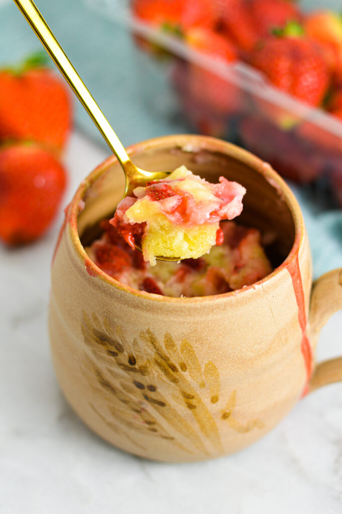 Strawberry Mug Cake with a gold spoon taking a piece out.