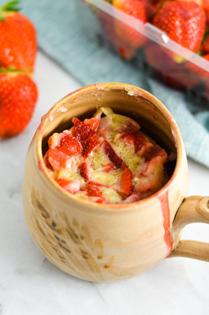 Strawberry Mug Cake in a beige mug with fresh strawberries in the background.