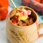 A Strawberry Mug Cake on a white granite surface with juicy fresh strawberries in the background.