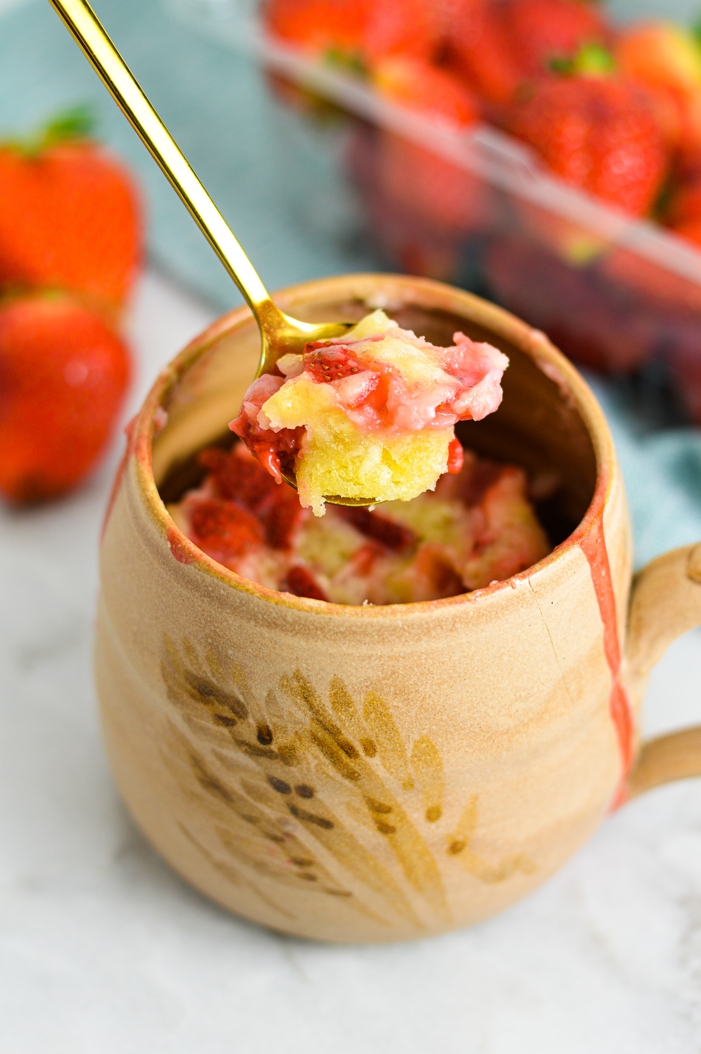 A Strawberry Mug Cake on a white granite surface with juicy fresh strawberries in the background.