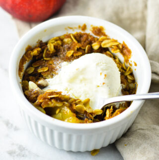 5 Minute Apple Crisp for One with a scoop of vanilla ice cream on top and a spoon in the white ramekin.