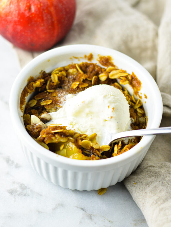 5 Minute Apple Crisp for One with a scoop of vanilla ice cream on top and a spoon in the white ramekin.