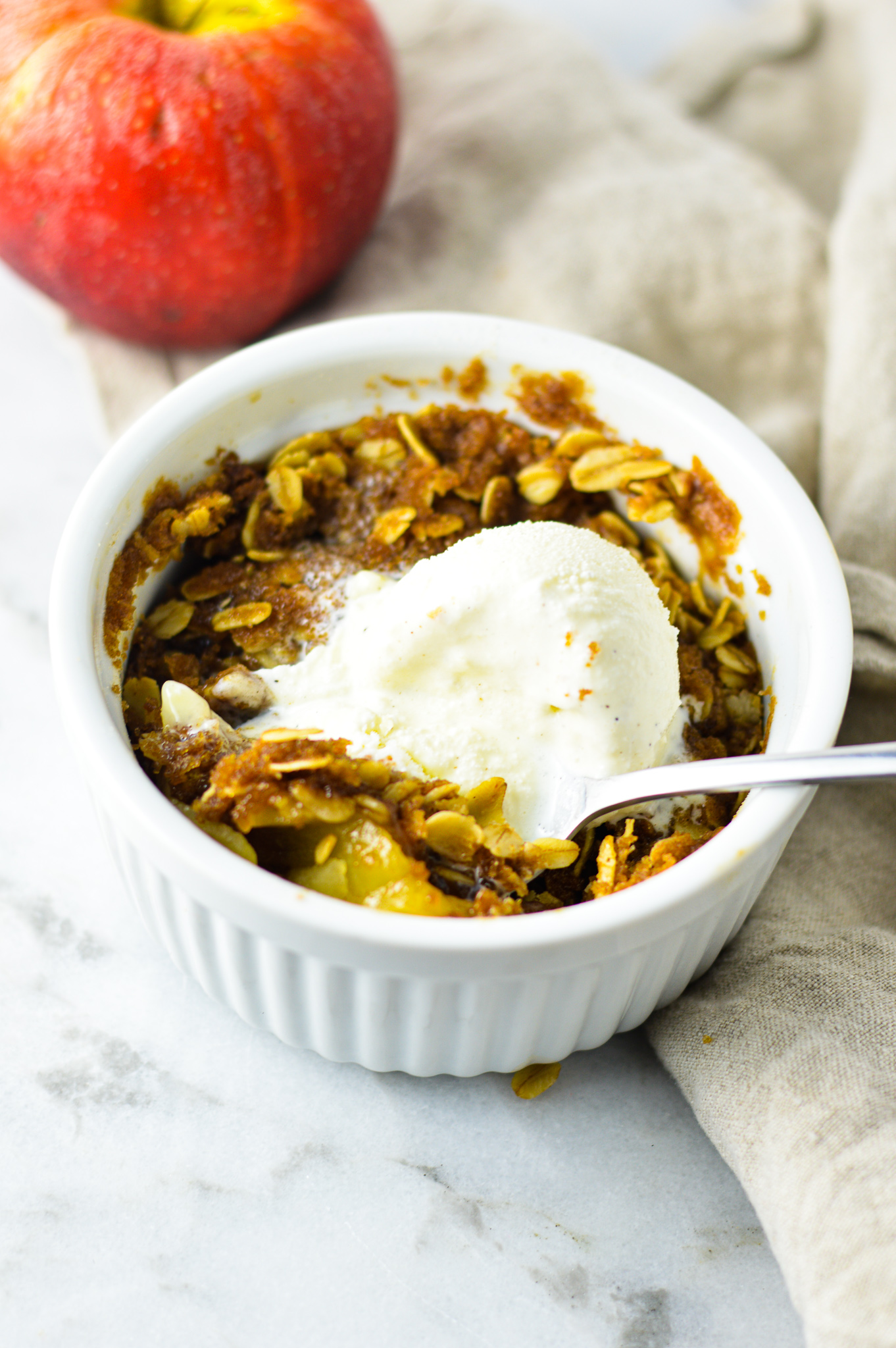 5 Minute Apple Crisp for One with a scoop of vanilla ice cream on top and a spoon in the white ramekin.