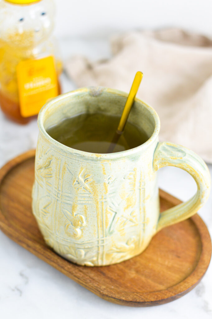 Apple Cider Vinegar Tea with a small gold spoon in the mug with honey in the background.