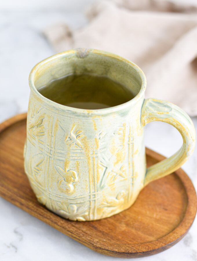 Apple Cider Vinegar Tea in a large green ceramic mug on a small wooden surface.