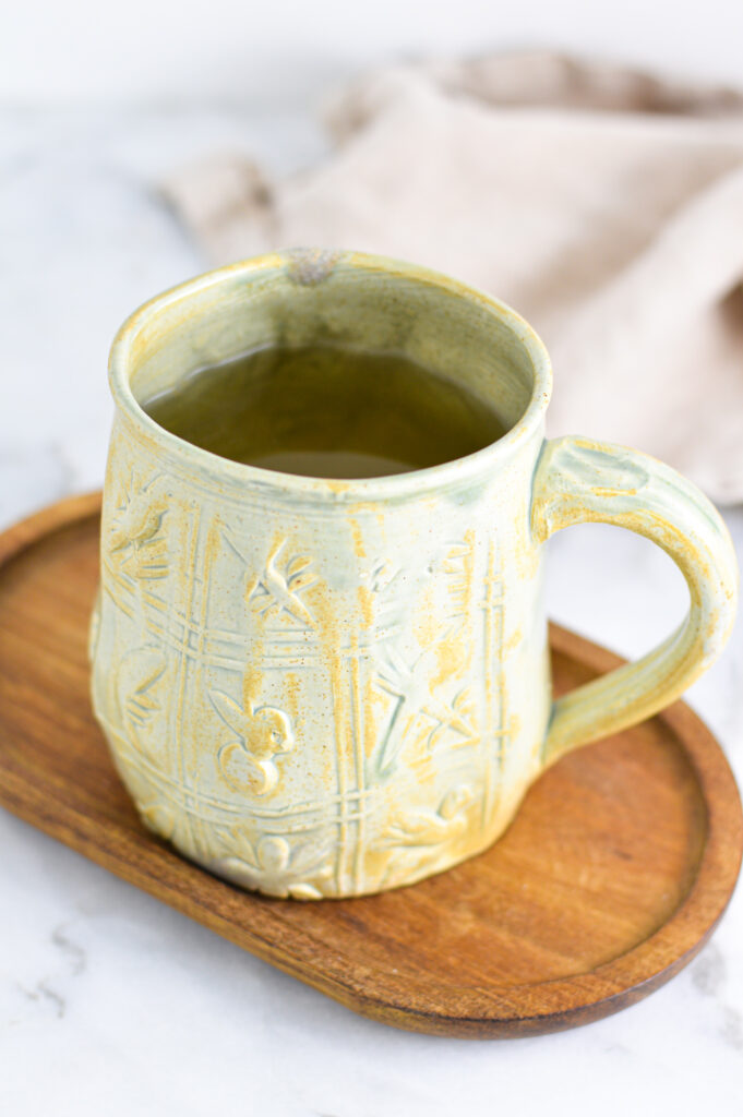 Apple Cider Vinegar Tea in a large green ceramic mug on a small wooden surface.