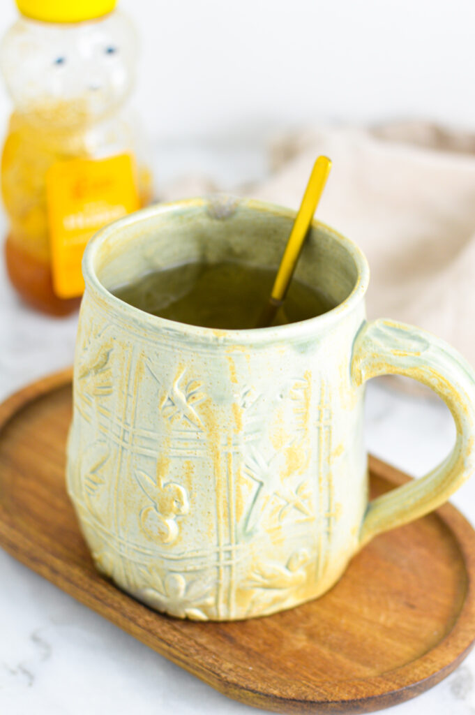 Apple Cider Vinegar Tea with a golden teaspoon in the large ceramic mug on a small wooden tray.