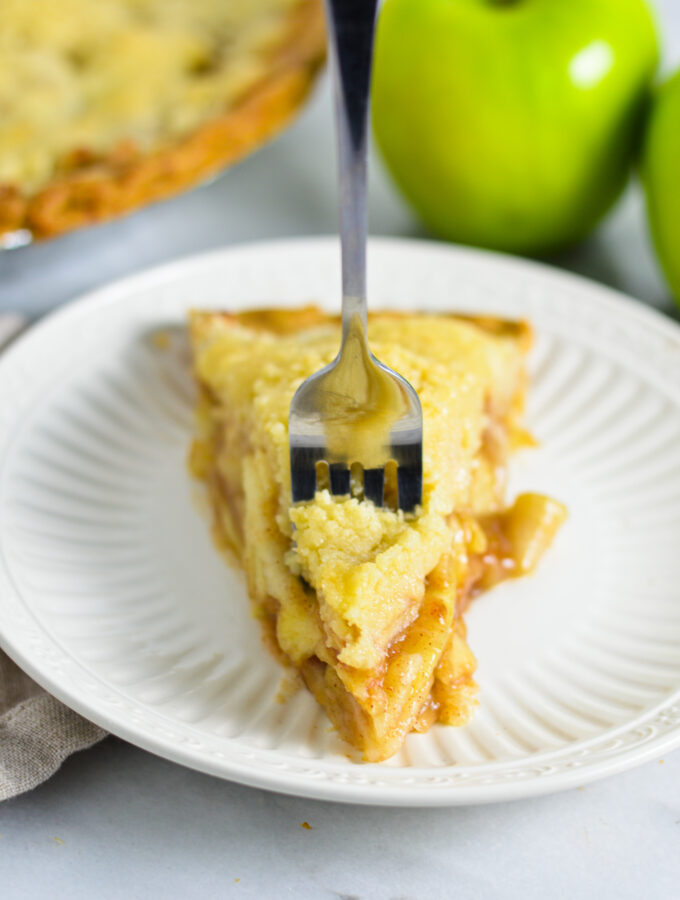 A fork in a slice of Butter Crumble Apple Pie on a white plate.