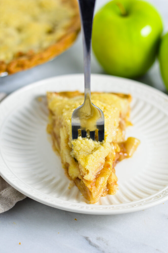 A fork in a slice of Butter Crumble Apple Pie on a white plate.