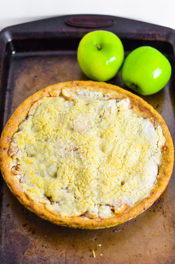 Butter Crumble Apple Pie on a baking sheet with two Granny Smith apples in the background.