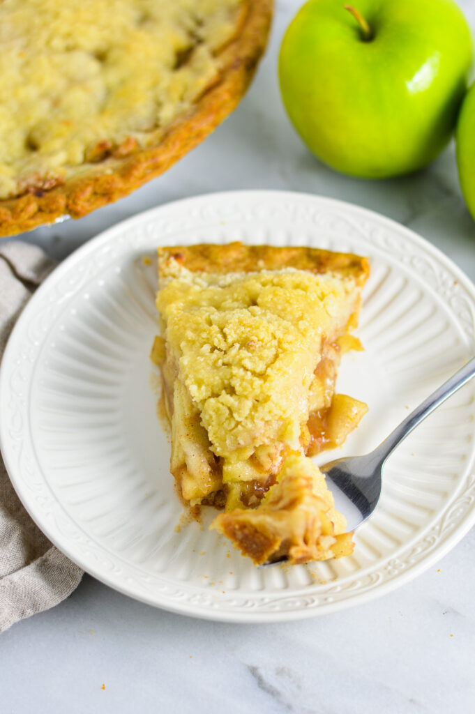 A slice of Butter Crumble Apple Pie with a fork on a white dessert plate.