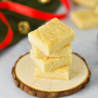 A stack of golden Shortbread Cookies on a wooden surface with a red ribbon and gold bells in the background, giving a Christmas feeling.