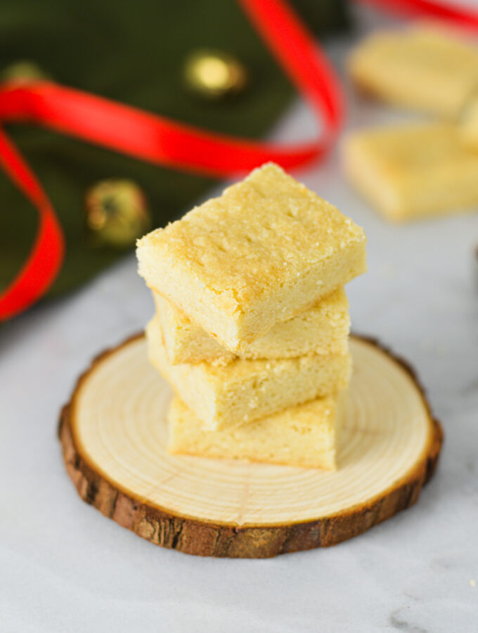 A stack of golden Shortbread Cookies on a wooden surface with a red ribbon and gold bells in the background, giving a Christmas feeling.