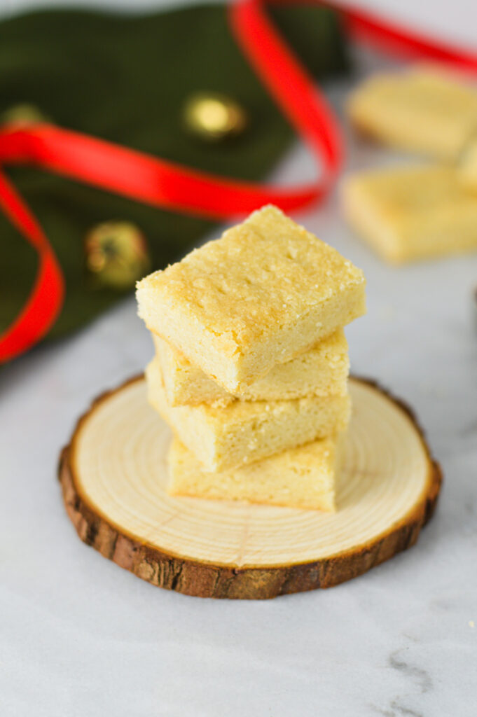 A stack of golden Shortbread Cookies on a wooden surface with a red ribbon and gold bells in the background, giving a Christmas feeling.