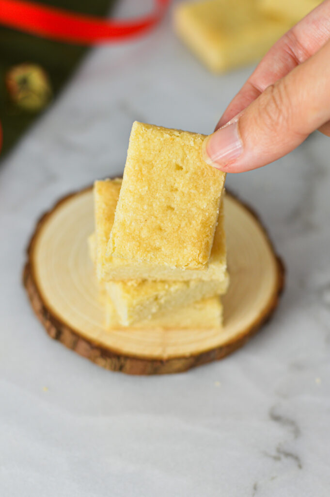 A hand taking a Shortbread Cookie from a stack, with some fork marks on top of the golden cookie.