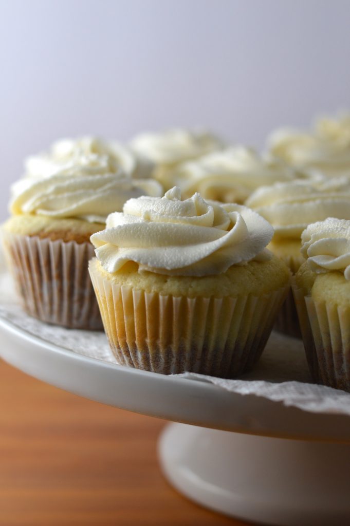 Super moist vanilla cupcakes with vanilla frosting. A surprise cookie is baked on the bottom of the cupcakes to make them extra special.