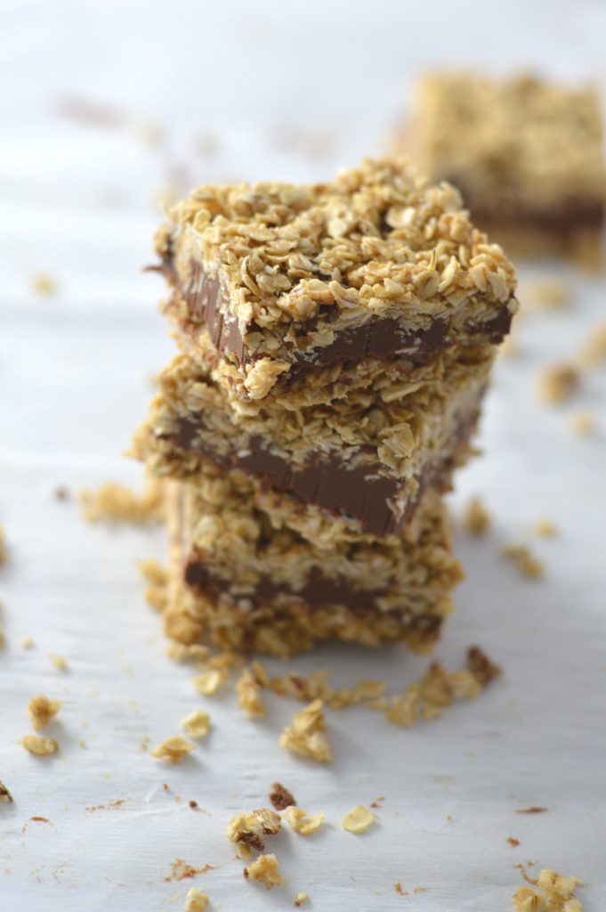 A stack of 3 No Bake Peanut Butter and Chocolate Oat Fudge Bars with quick oats sprinkled all around them.