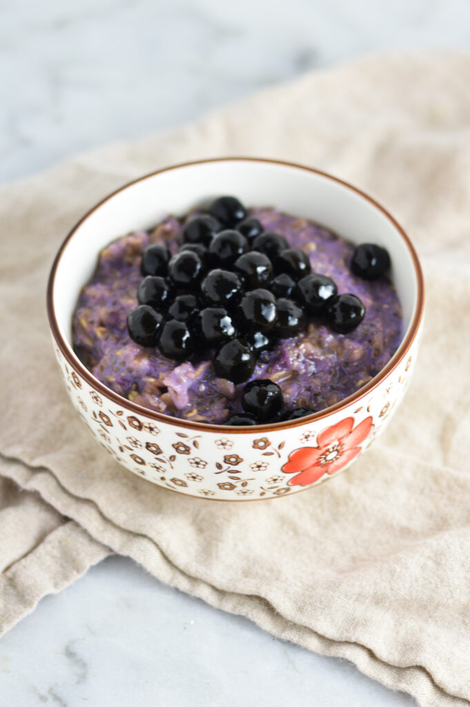 Taro Bubble Tea Oatmeal in a small bowl with flowers on a linen napkin.