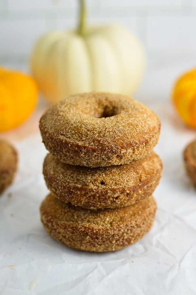 A small stack of Baked Apple Cider Donuts with white and orange mini pumpkins in the background.