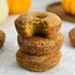 A stack of three Baked Apple Cider Donuts with some mini pumpkins in the background.