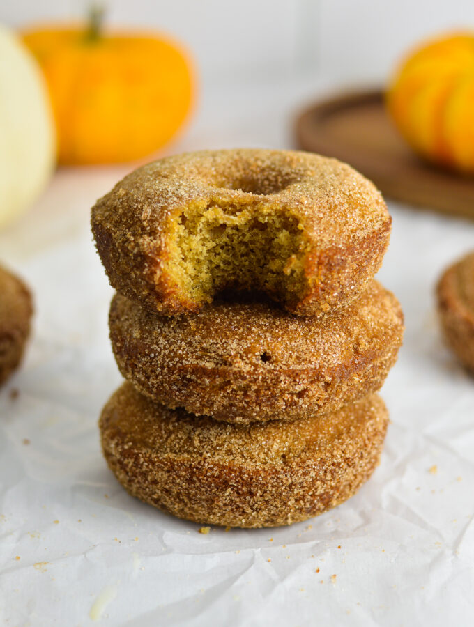 A stack of three Baked Apple Cider Donuts with some mini pumpkins in the background.