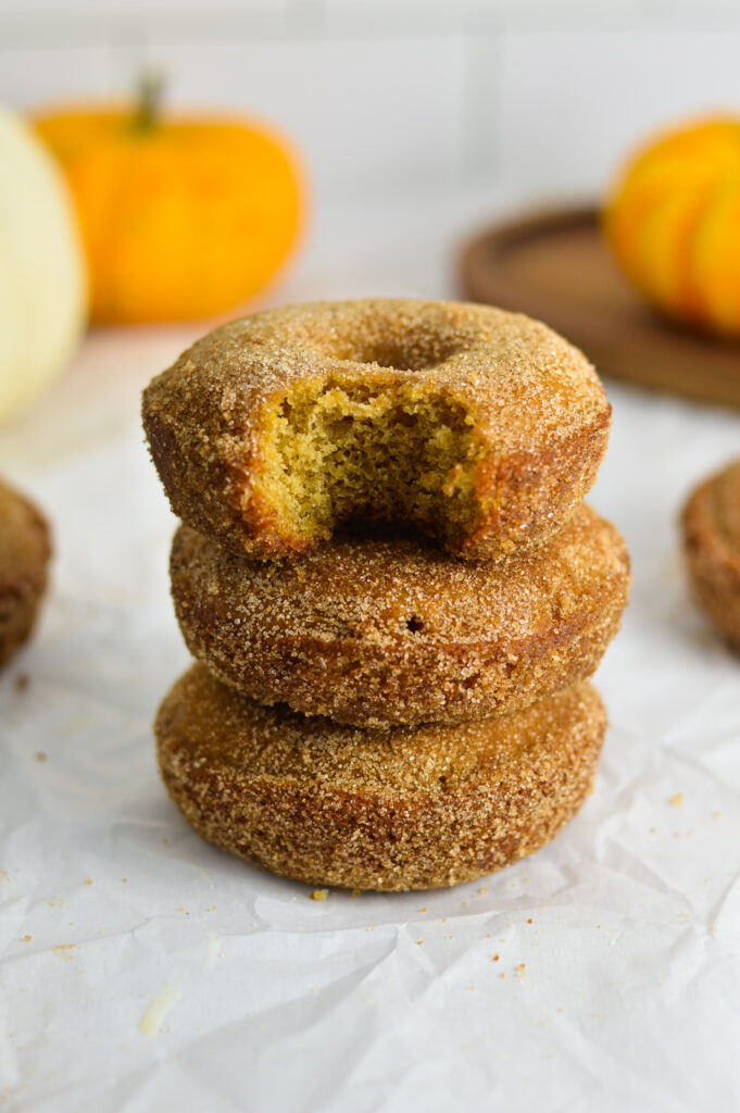 A stack of three Baked Apple Cider Donuts with some mini pumpkins in the background.