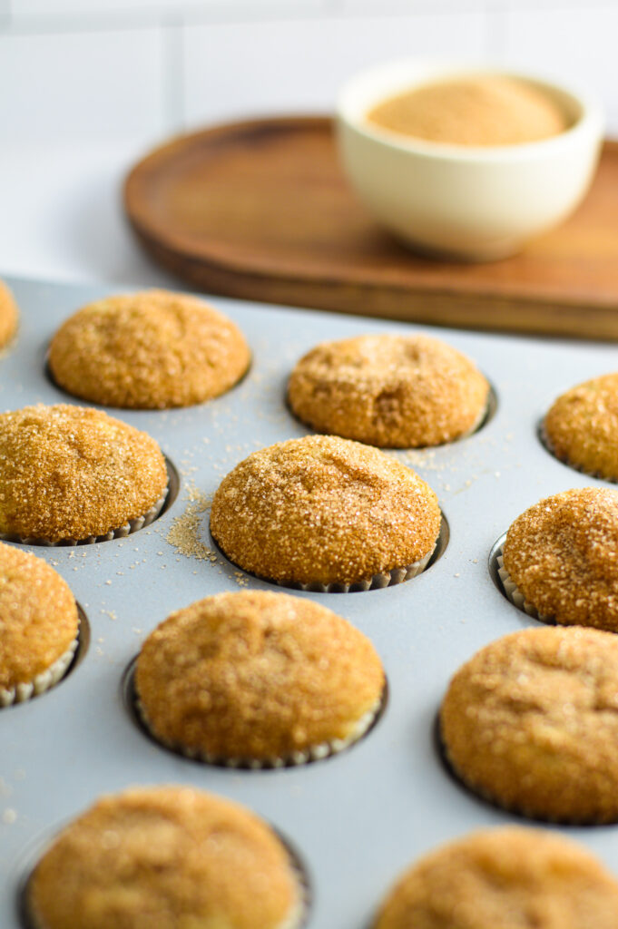 Mini Churro muffins in a mini muffin tin with a small bowl of cinnamon sugar on a wooden plank.