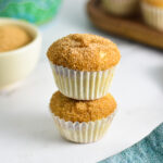 Two Churro Mini Muffins stacked with a coffee cup and a small bowl of cinnamon sugar in the background.