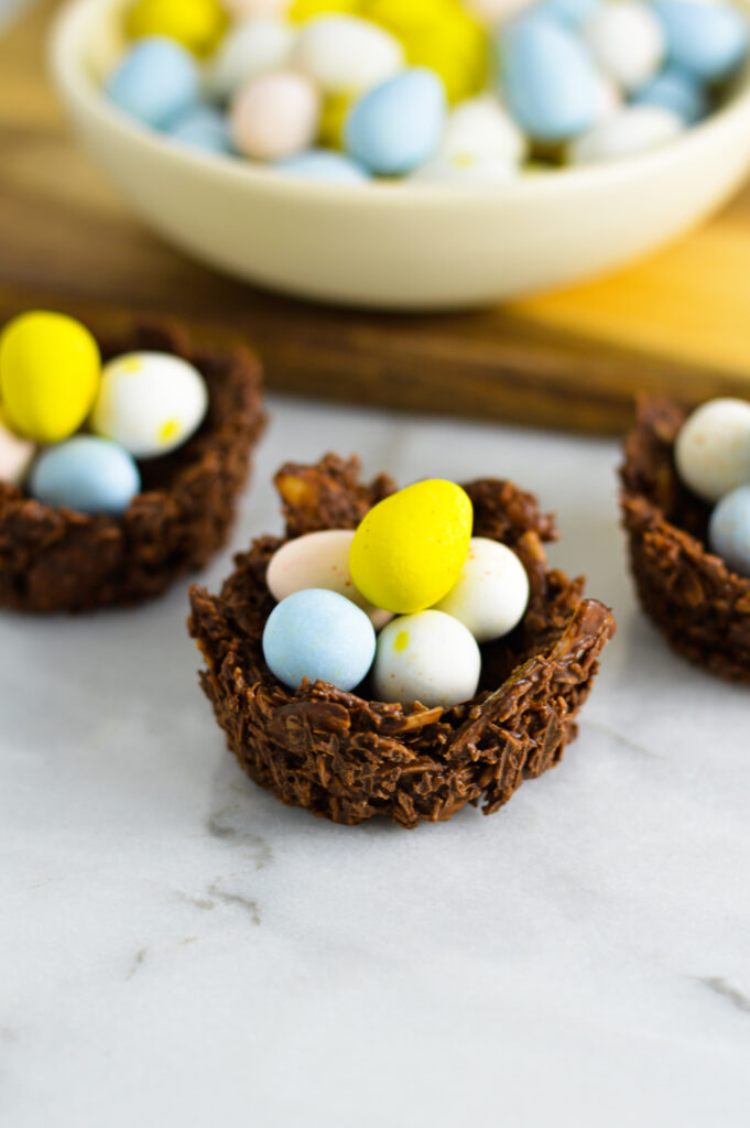 3 Almond Joy Easter Egg Nests with a small bowl of chocolate eggs on a wooden board.