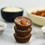 3 Almond Joy Nutella Cups stacked with a pinch bowl of coconut and a shallow white bowl of whole almonds in the background.