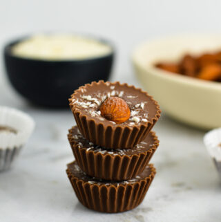 3 Almond Joy Nutella Cups stacked with a pinch bowl of coconut and a shallow white bowl of whole almonds in the background.