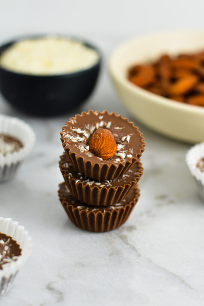 Stack of three Almond Joy Nutella Cups with small bowls of unsweetened shredded coconut and whole almonds in the background.