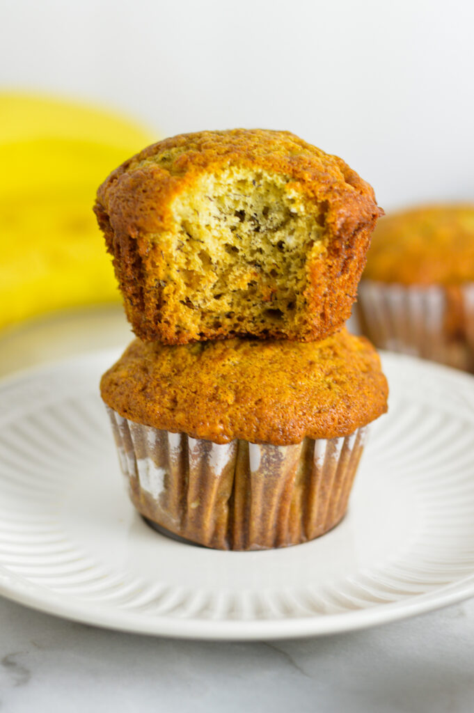 A stack of two Banana Muffins with a bite taken out of the top muffin.