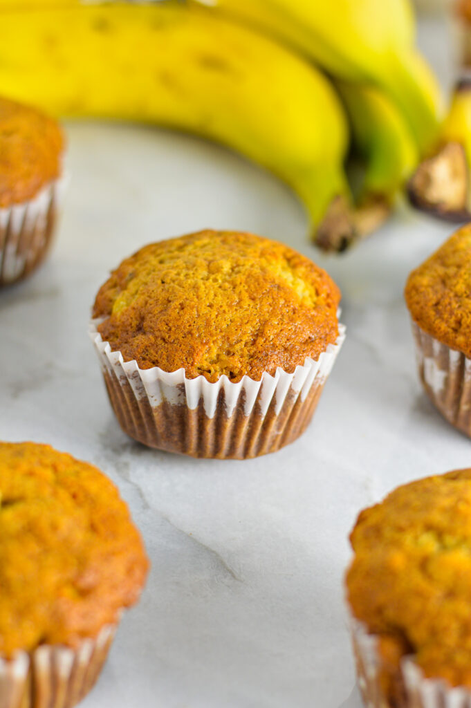 Banana Muffins on a granite surface with bananas in the background.