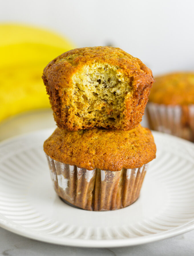 Two fluffy Banana Muffins stacked with a bite taken out of the top muffin.