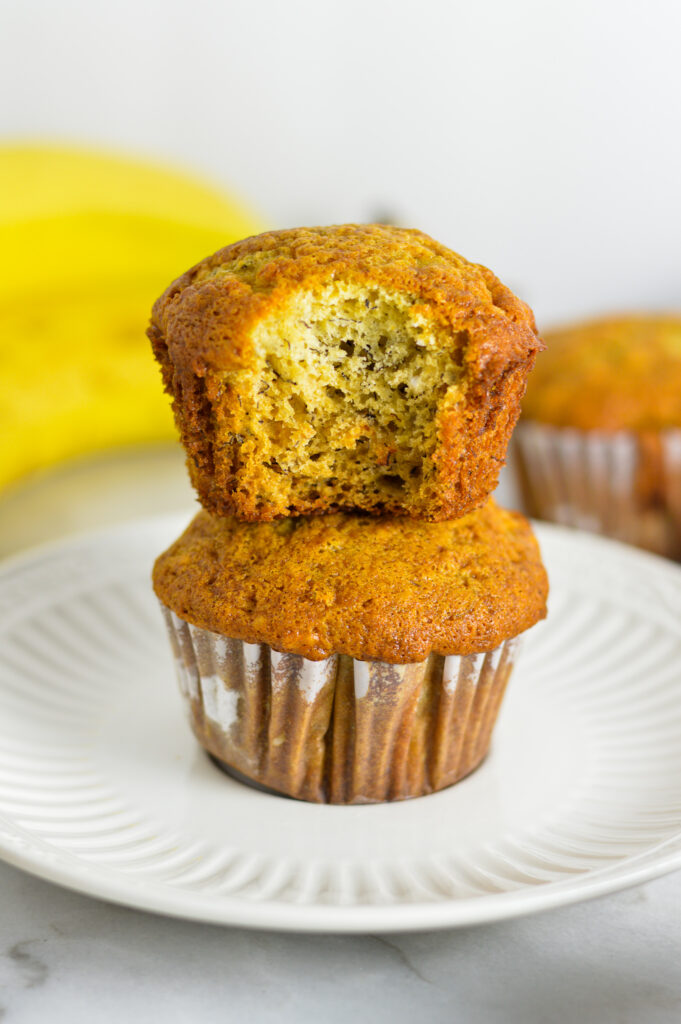 Two fluffy Banana Muffins stacked with a bite taken out of the top muffin.