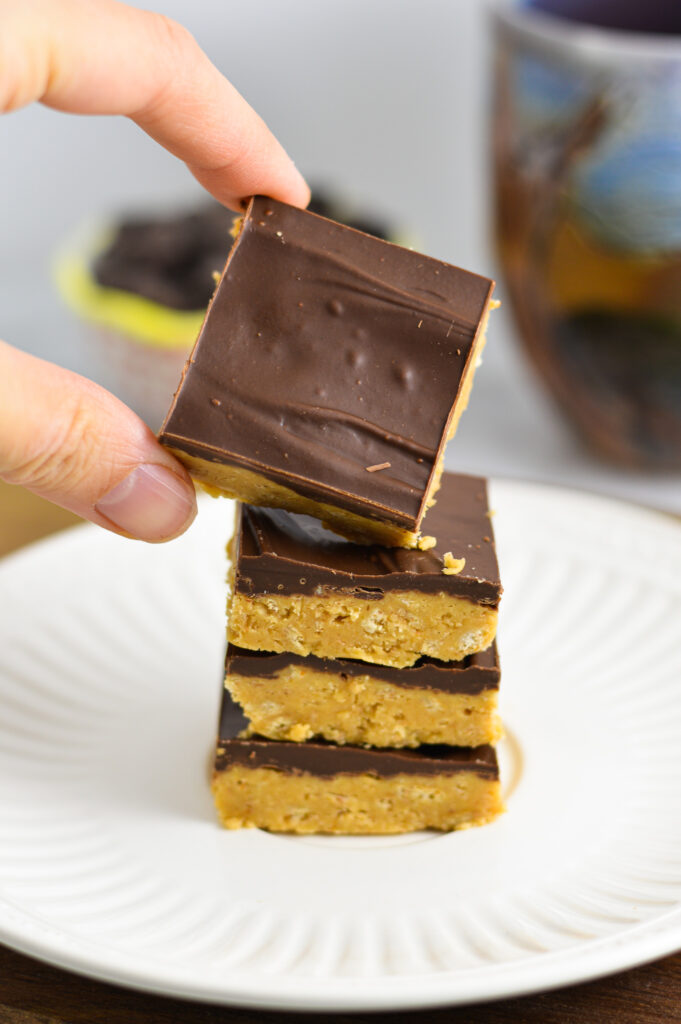 A hand showing a Peanut Butter Square with a Chocolate layer.